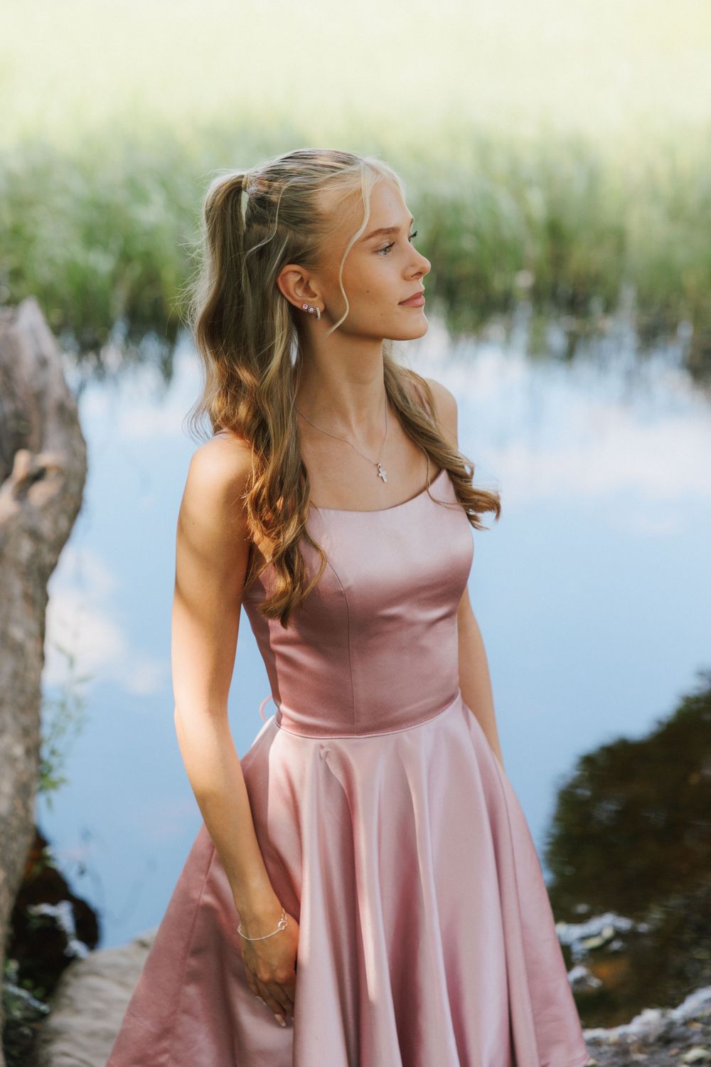 A pink satin dress flows elegantly against a tranquil lakeside background with soft natural lighting.