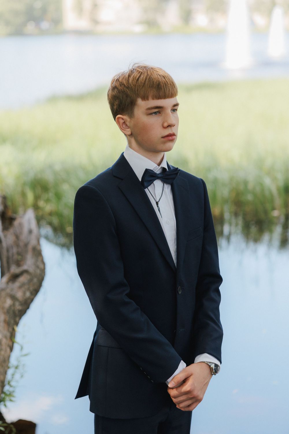 A person in a black tuxedo poses near a pond during formal portraits.
