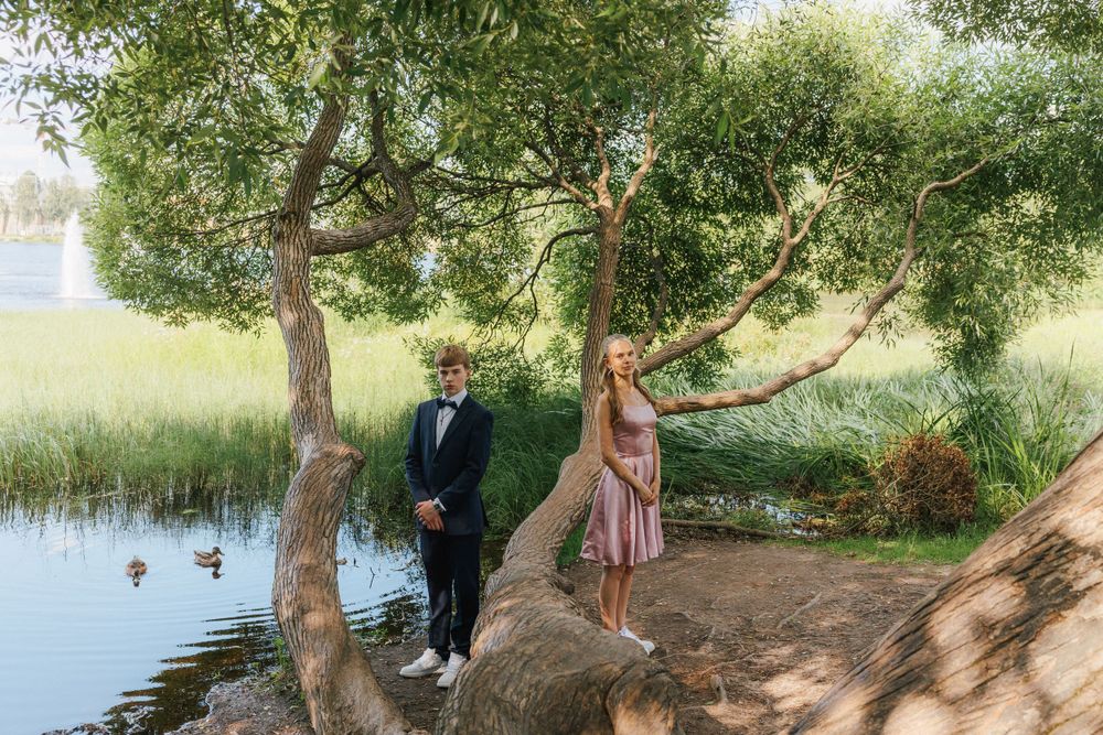 A couple enjoying a romantic moment by a tranquil pond with overhanging trees on a sunny day.
