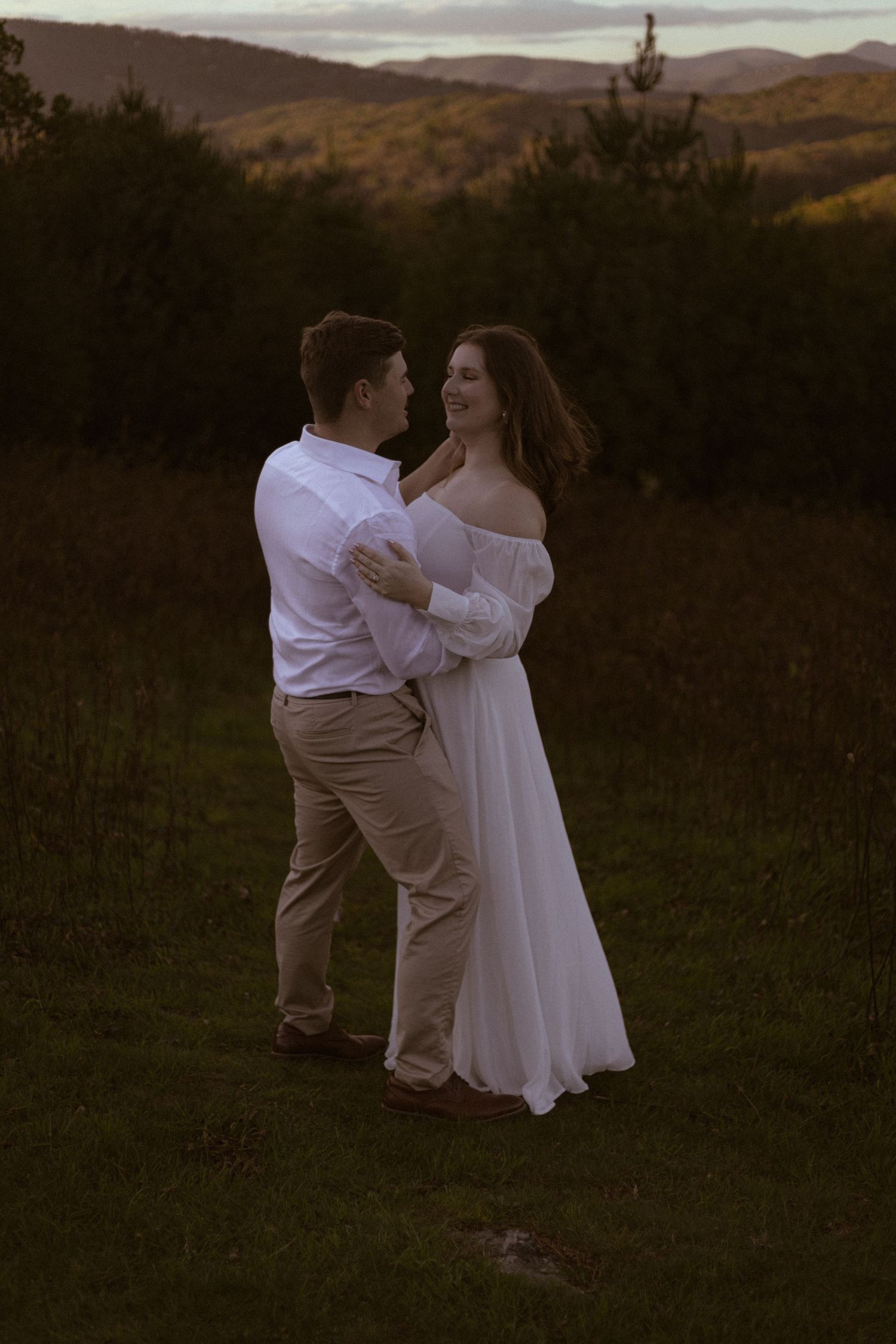 A couple embraces during sunset in a mountain field.