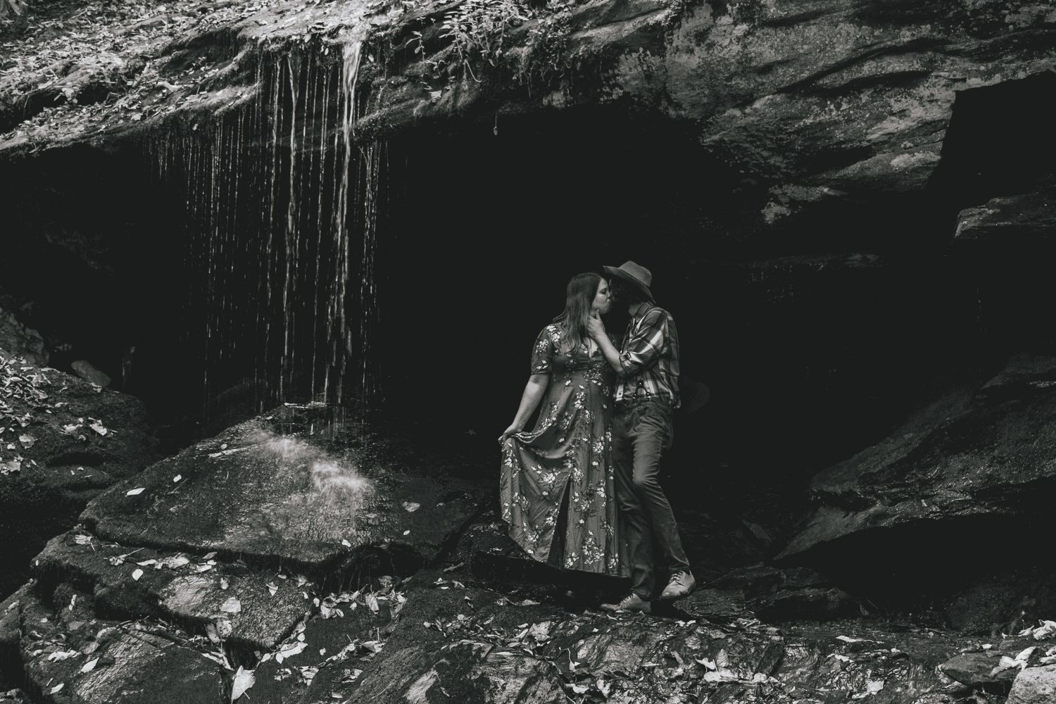 A romantic black and white photo captured in a cave with a waterfall in the background.