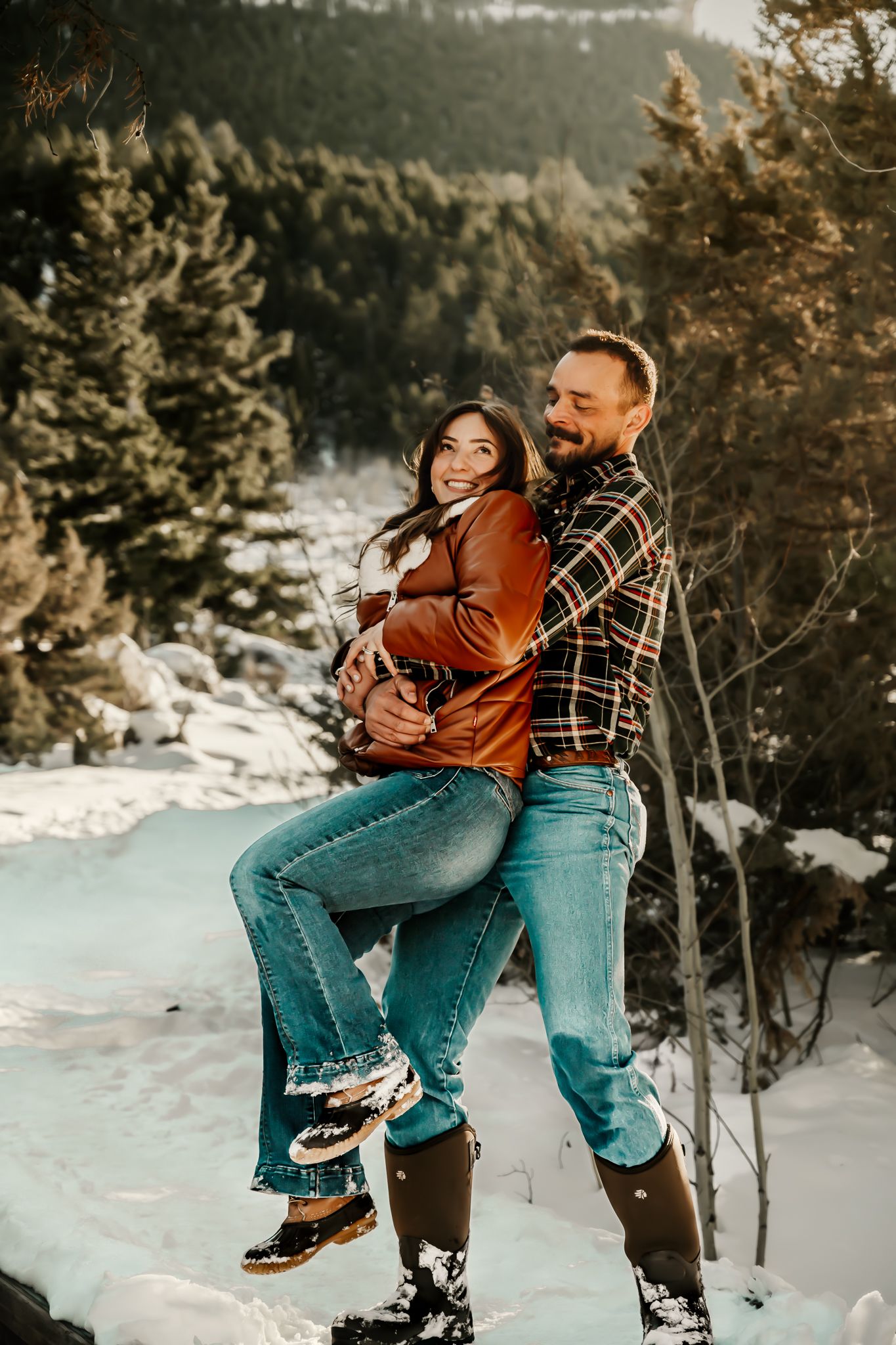Playful winter portrait of couple in plaid and denim against snowy mountain backdrop.