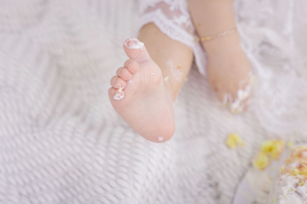 Close up view of a tiny baby foot on a white textured blanket with yellow flowers in the background.