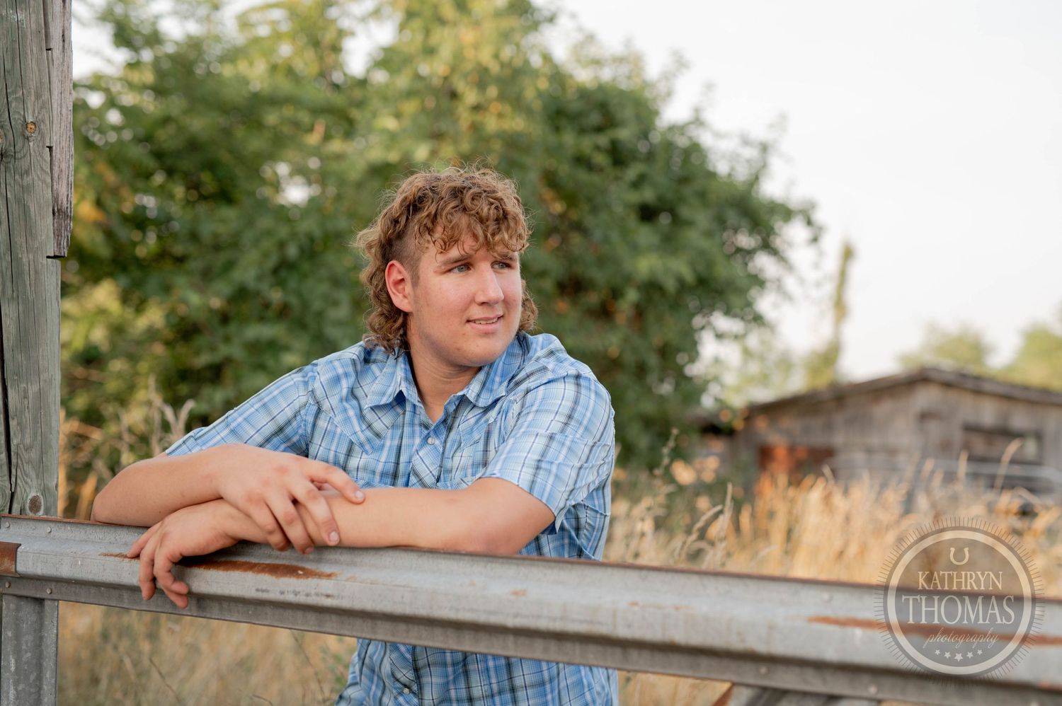 A casual portrait leaning on a wooden fence rail with trees in the background.