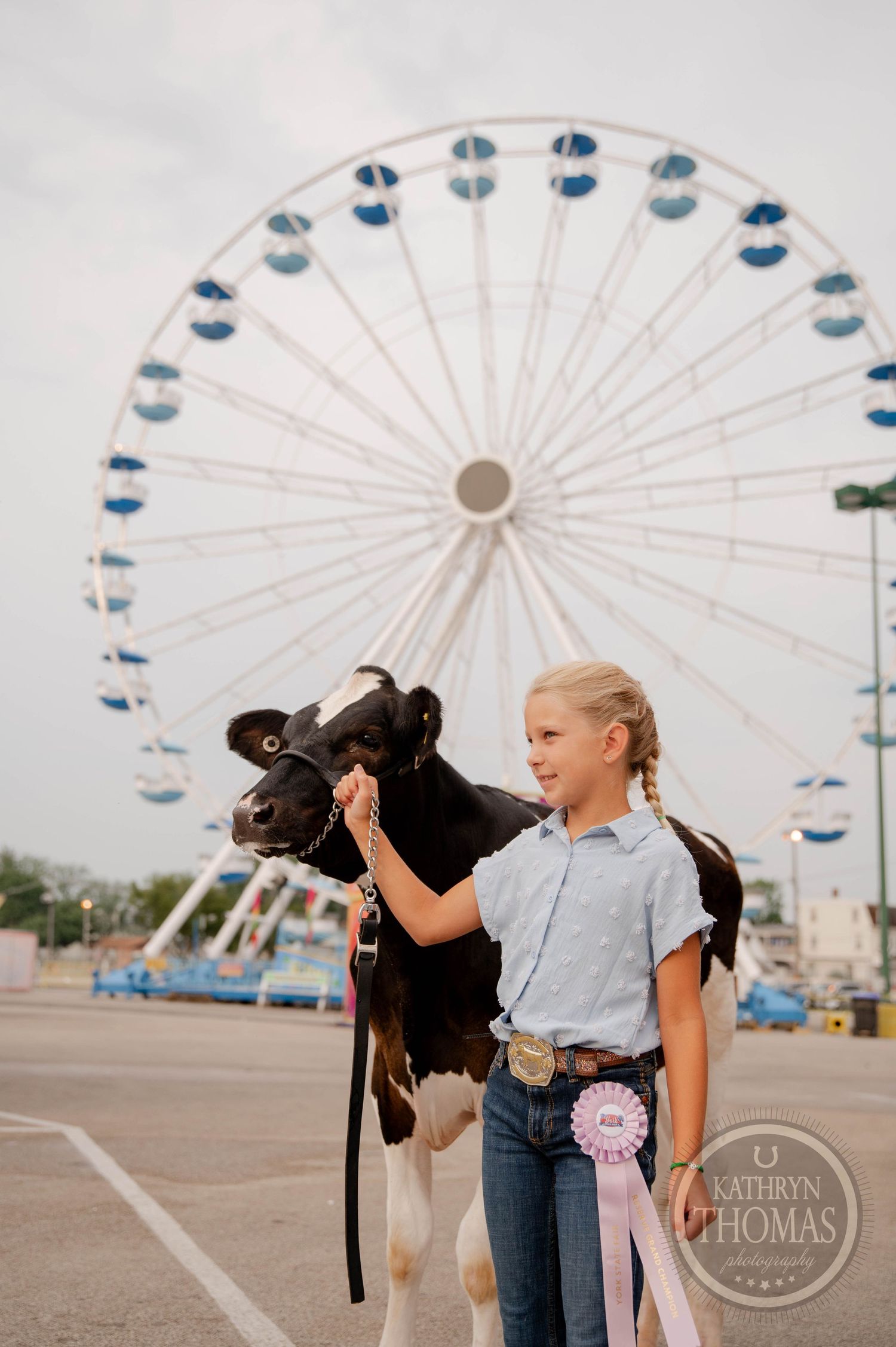 Young exhibitor with dairy calf standing in front of large ferris wheel at fairgrounds.