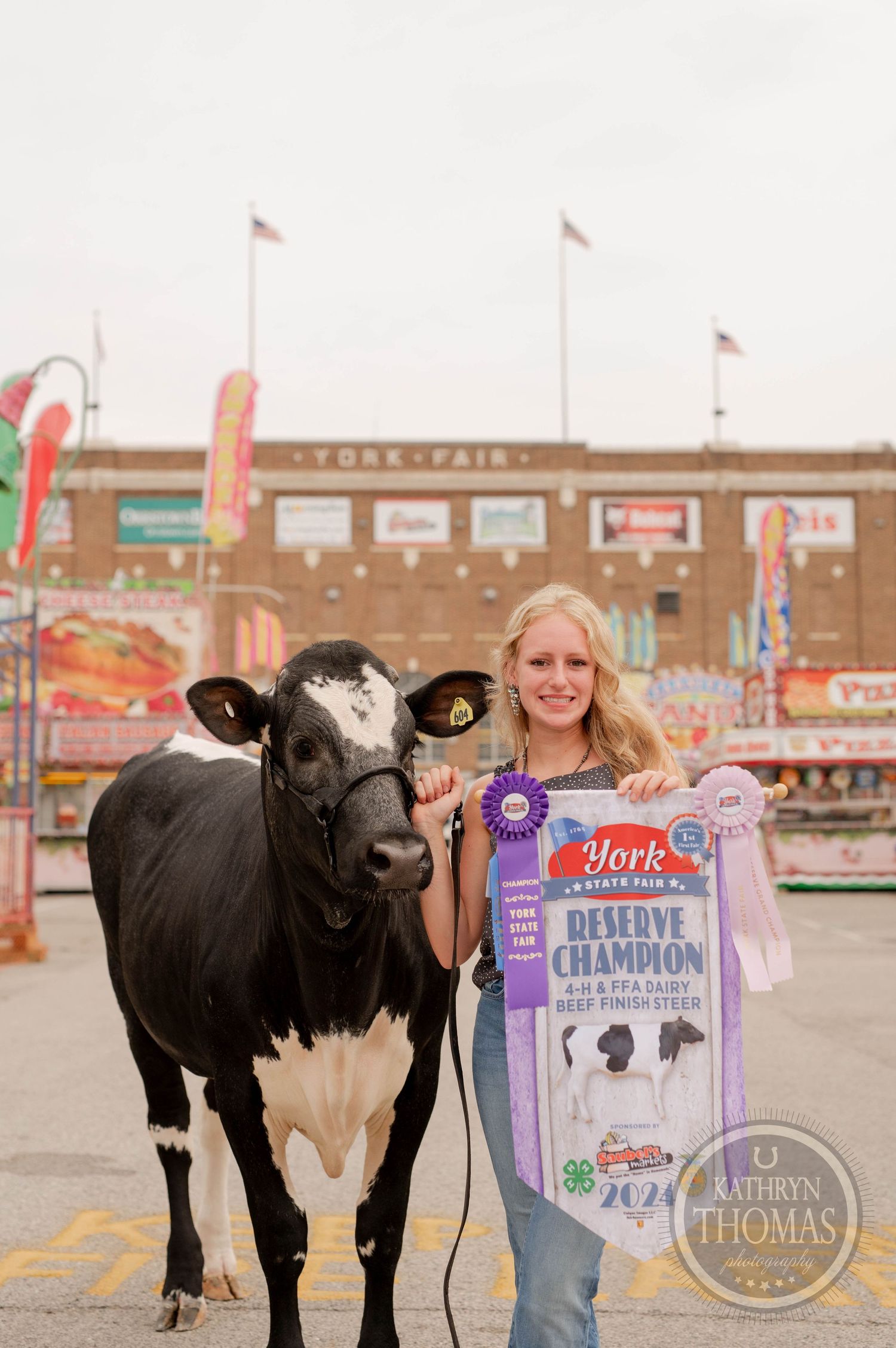 Black and white dairy cow poses with champion ribbon at county fair.