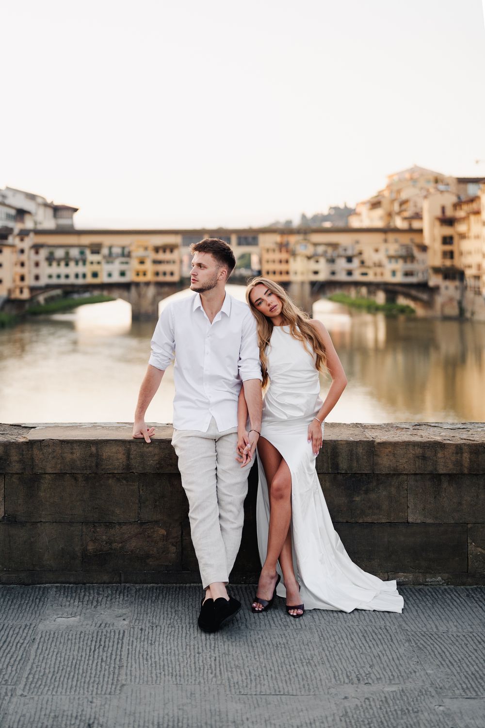 Narzeczeni pozują na tle Ponte Vecchio, Florencja, długa biała suknia, luksusowa i romantyczna sesja narzeczeńska w mieście sztuki.
