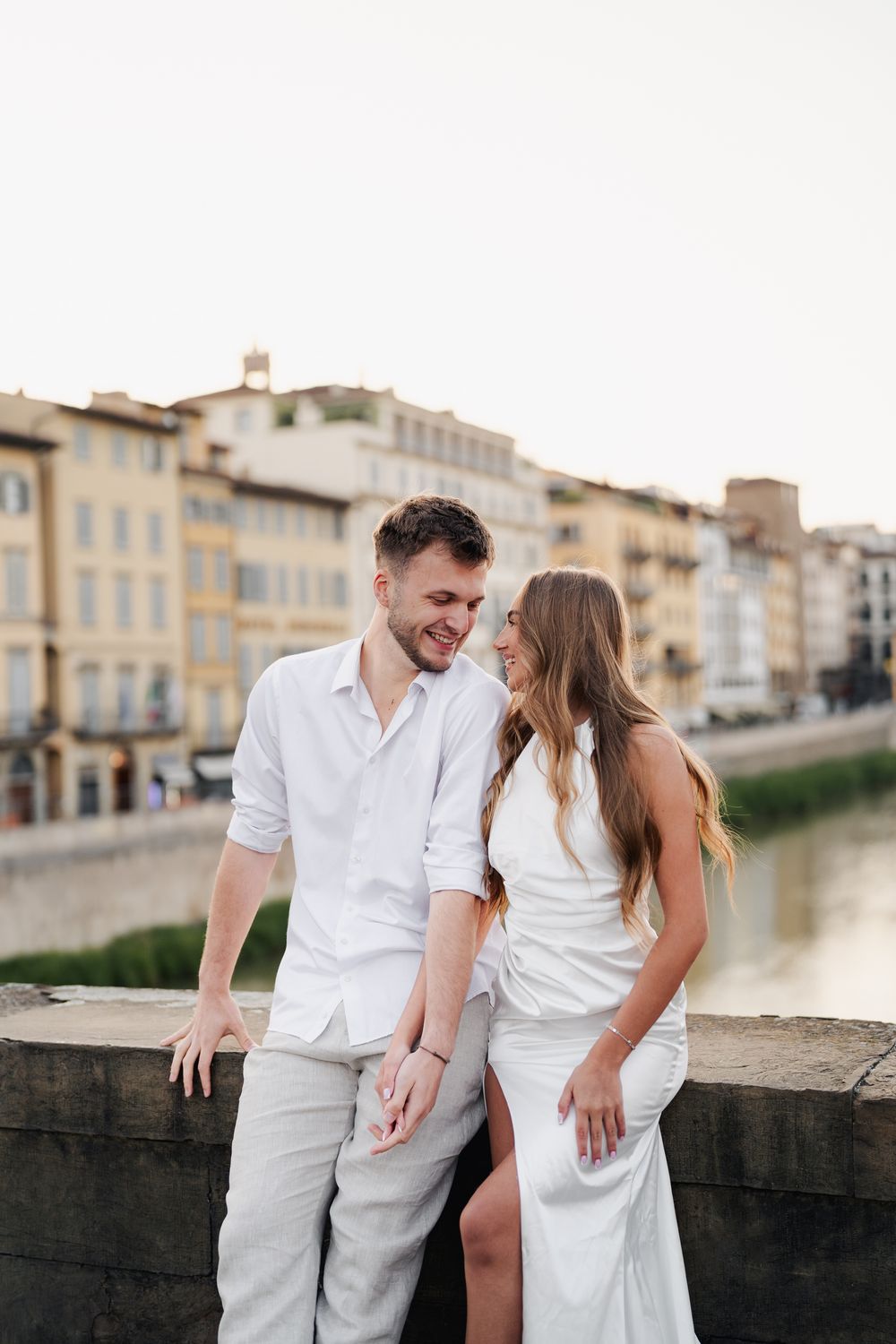 Narzeczeni stojący na moście Ponte Vecchio we Florencji, wschodzące słońce maluje ciepłe światło na ich twarzach, pełnych uśmiec
