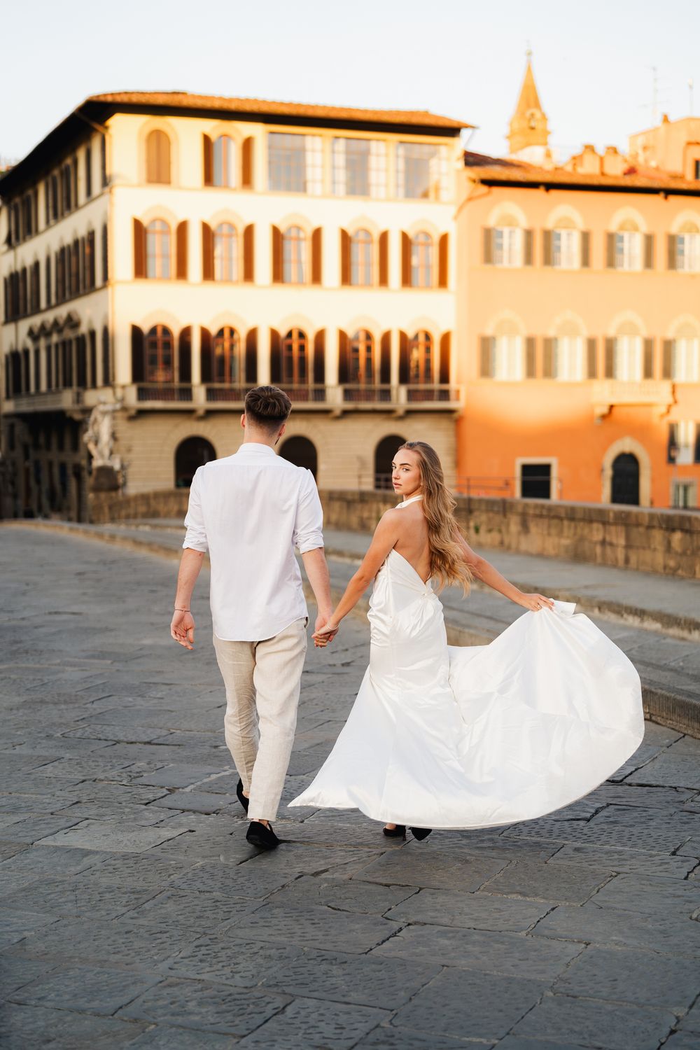 Romantyczna sesja narzeczeńska we Florencji, para młoda spaceruje po moście Ponte Vecchio o wschodzie słońca.