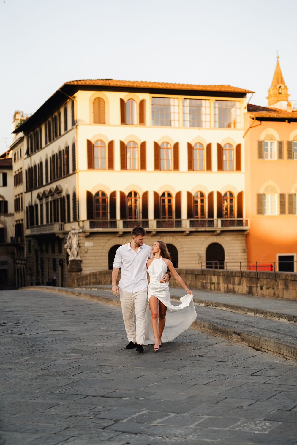 Narzeczeni spacerują po historycznym moście Ponte Vecchio we Florencji, wschodzące słońce podkreśla ich miłość i radość.
