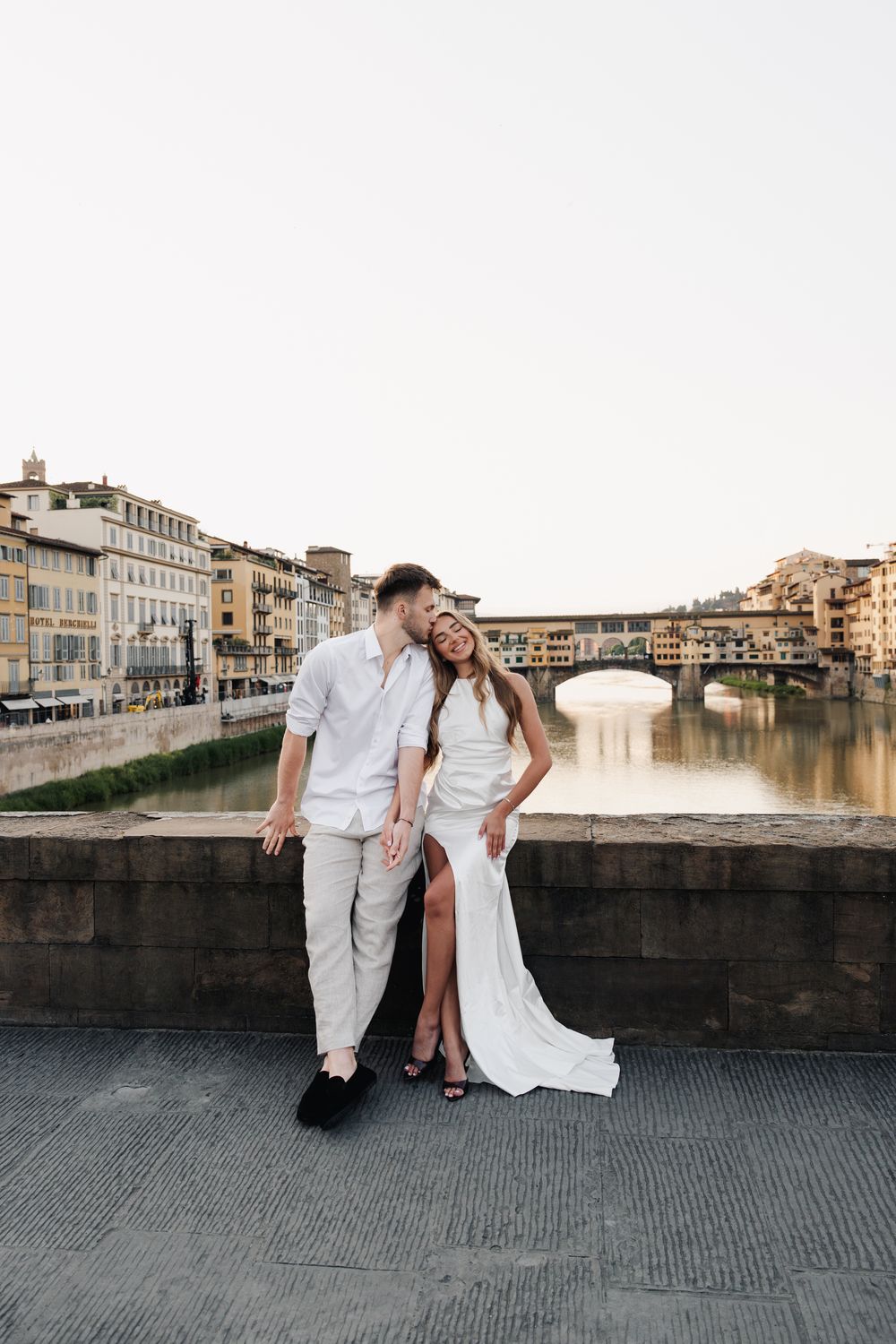 Romantyczna sesja narzeczeńska we Florencji o wschodzie słońca, para patrzy sobie w oczy, rzeka Arno i Ponte Vecchio tworzą piękne tło.