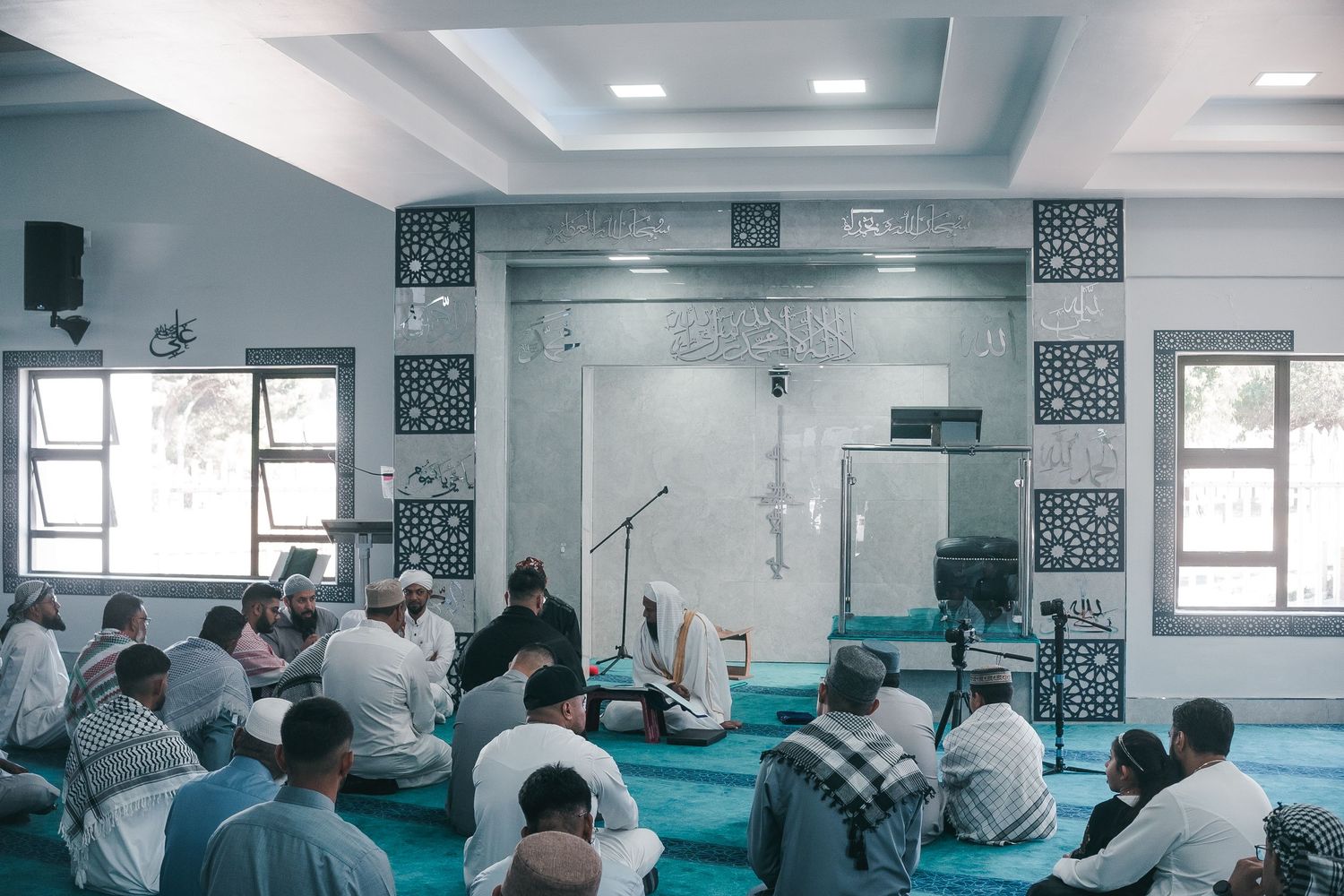 Interior of a mosque with turquoise prayer carpet and decorative Islamic patterns on the walls.