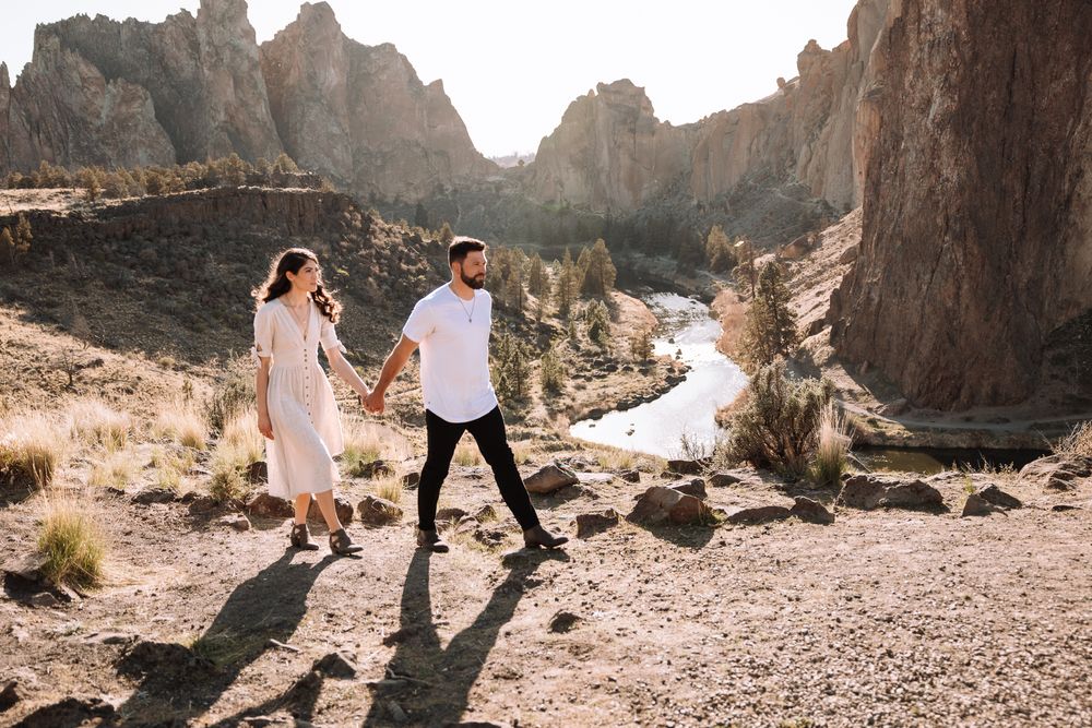 A couple walking hand in hand through a dramatic desert canyon landscape.