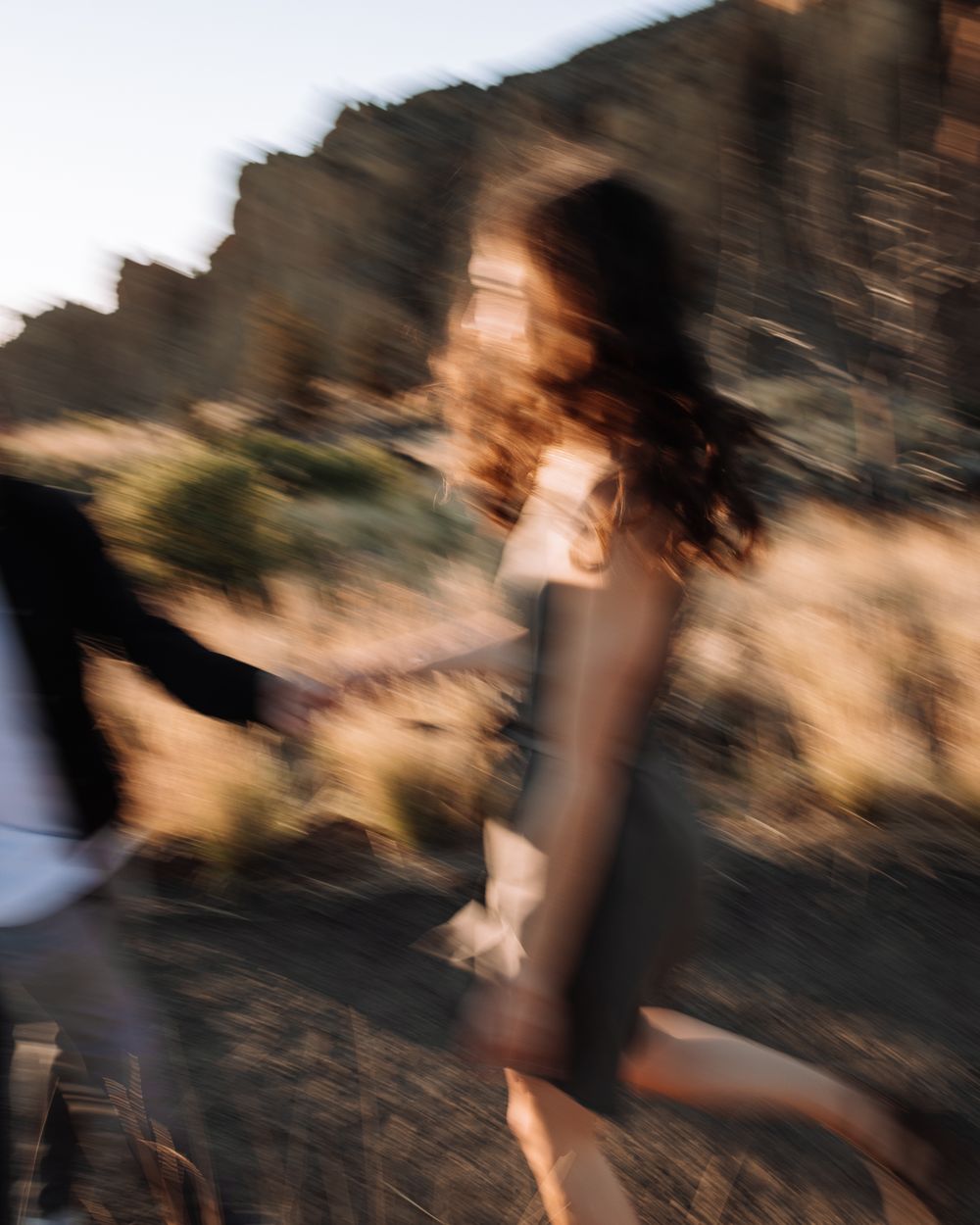 Motion-blurred artistic photo of a person spinning in a flowing dress at sunset against a rocky landscape.