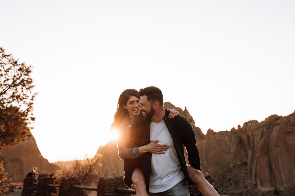 A couple embraces against a warm sunset backdrop with rocky cliffs in Smith Rock State Park, Oregon.