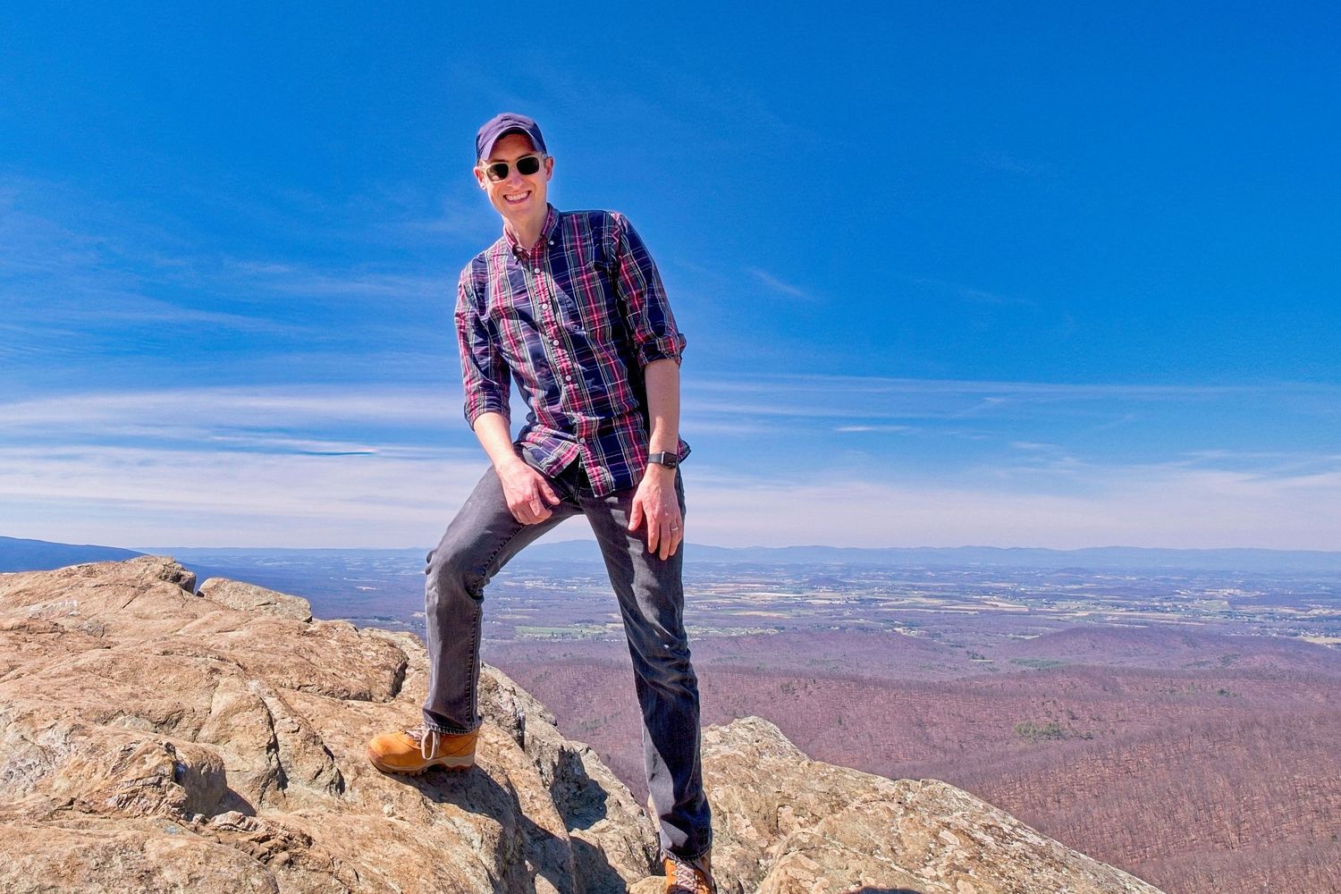 A figure stands victoriously on a rocky mountain summit against a vast desert landscape.