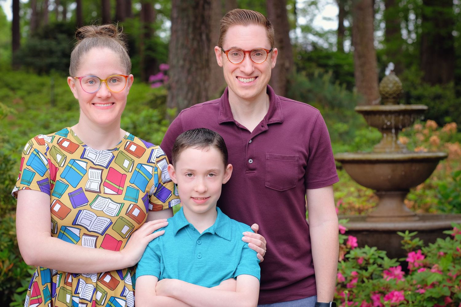 A colorful family portrait taken outdoors with a decorative fountain and garden in the background.