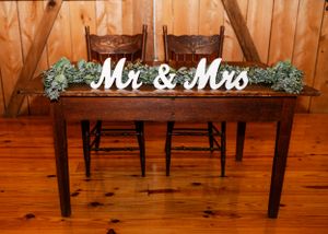 Rustic wooden sweetheart table with 'Mr & Mrs' sign and greenery decorations at a wedding reception.