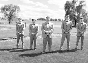 Black and white photo of groomsmen in formal attire standing in line on grass field.