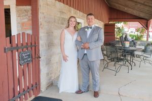 Wedding couple poses under rustic red barn overhang during countryside celebration.