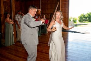Wedding couple dances together on wooden floor during rustic barn reception.
