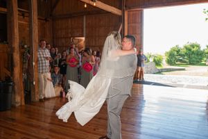 Couple sharing romantic dance together in rustic wooden barn venue with flowing white dress.