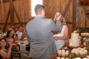 A couple shares their first dance as newlyweds next to their wedding cake in a rustic wooden barn reception venue.