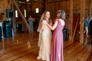 Two people in formal gowns share an intimate moment on a wooden dance floor inside a rustic barn venue.