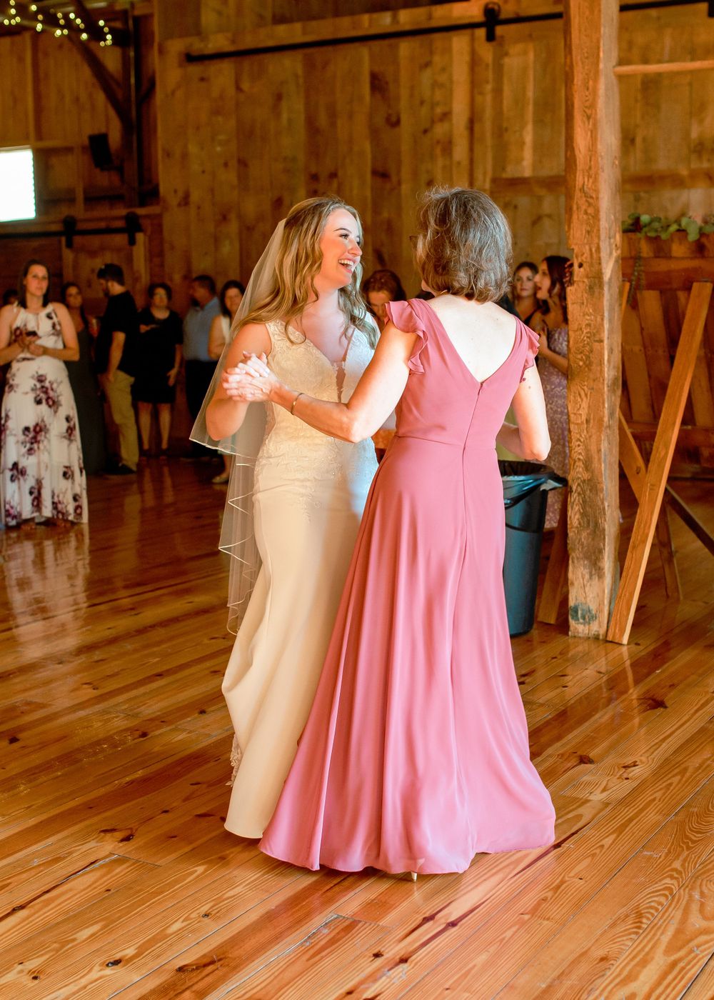 Wedding celebration with dancers in white and pink gowns sharing a moment on a rustic wooden dance floor in a barn.