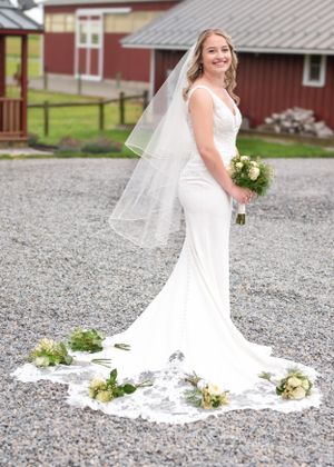 A stunning white wedding dress with a long lace train and veil against a rustic barn backdrop.