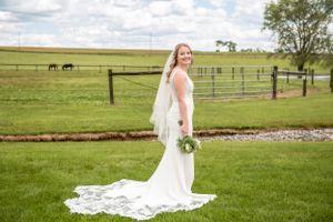 A white wedding gown with flowing train photographed in a countryside setting with horses in the background.