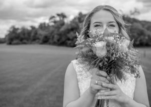 Black and white portrait of a joyful bride holding her wedding bouquet of delicate flowers against a pastoral backdrop.
