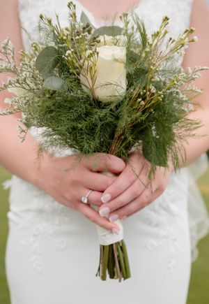 A rustic wedding bouquet featuring a single white rose surrounded by delicate greenery and wildflowers.