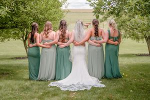 A group stands outdoors in varying shades of green and gray gowns, posing with their backs facing the camera.