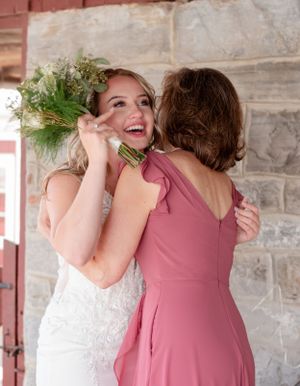 Two people sharing an emotional embrace at a wedding, with one wearing a white gown and the other in a dusty rose dress.