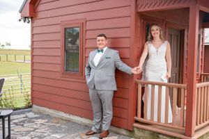 A couple shares a sweet first look moment outside a rustic red farmhouse with white trim.
