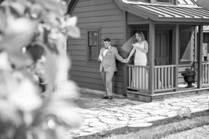 A black and white photo showing figures standing on a rustic front porch of a small house.