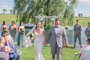 Beautiful outdoor wedding ceremony with guests seated on white chairs under a weeping willow tree.