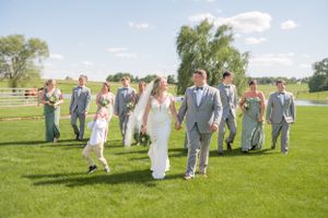 A wedding party walks together across a sunny green lawn on a beautiful summer day.