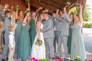 Wedding party celebrates with raised arms on a decorated outdoor venue stage.