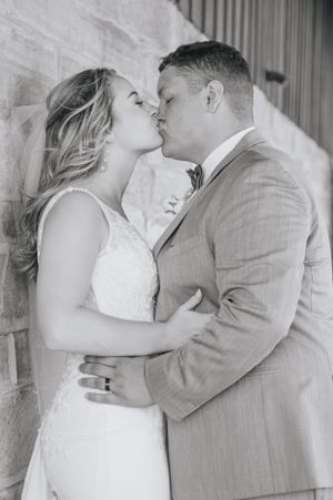 A tender black and white wedding photo of a couple sharing a romantic kiss against a brick wall.
