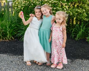 Three young girls in summer dresses pose together in garden setting.