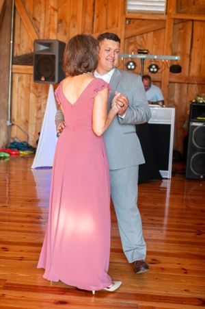 A couple dances together at a rustic wedding reception venue with wood paneled walls and hardwood floors.