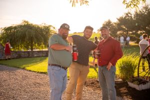 Three guests enjoying drinks and conversation during outdoor sunset reception.