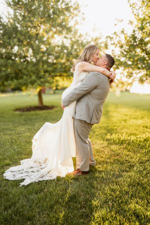 A couple shares a romantic embrace on their wedding day in a sunlit outdoor setting with flowing white dress.