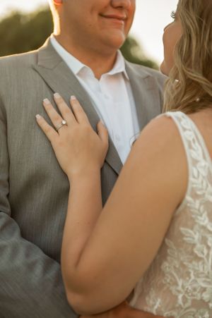 Close-up shot of bride's hand with engagement ring resting on groom's grey suit.
