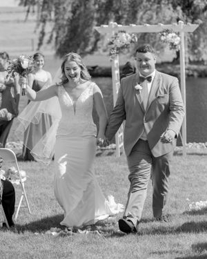 A happy couple walks down a garden path under a floral arch after their outdoor wedding ceremony.