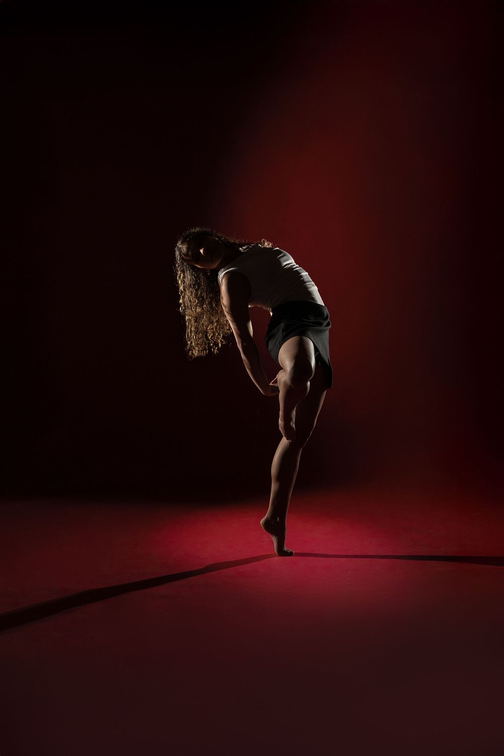Silhouette of a dancer performing dynamic movements against a dark red background in a dramatic photo series.
