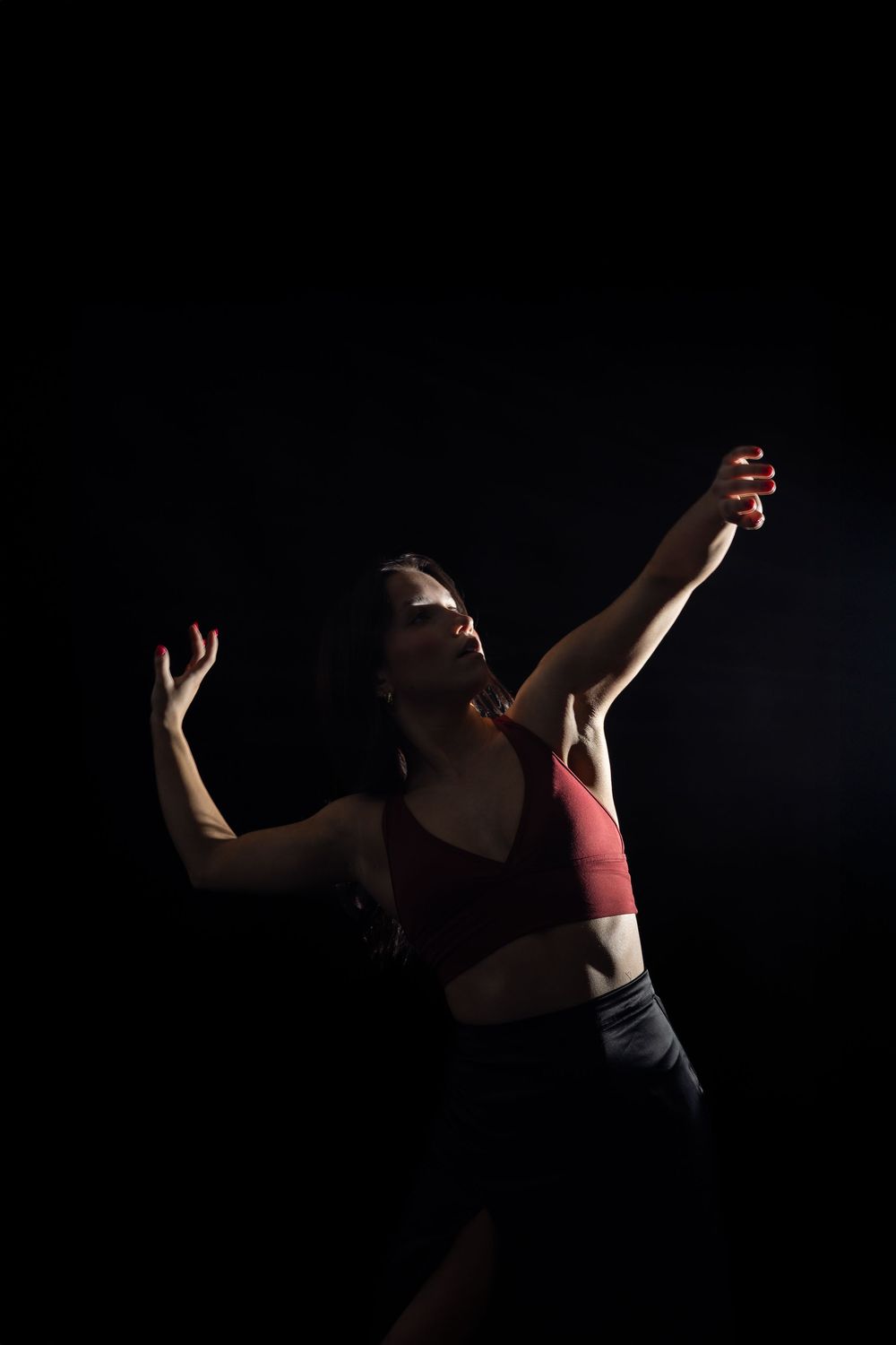 A dancer in a red top performs an expressive movement sequence against a dark background.