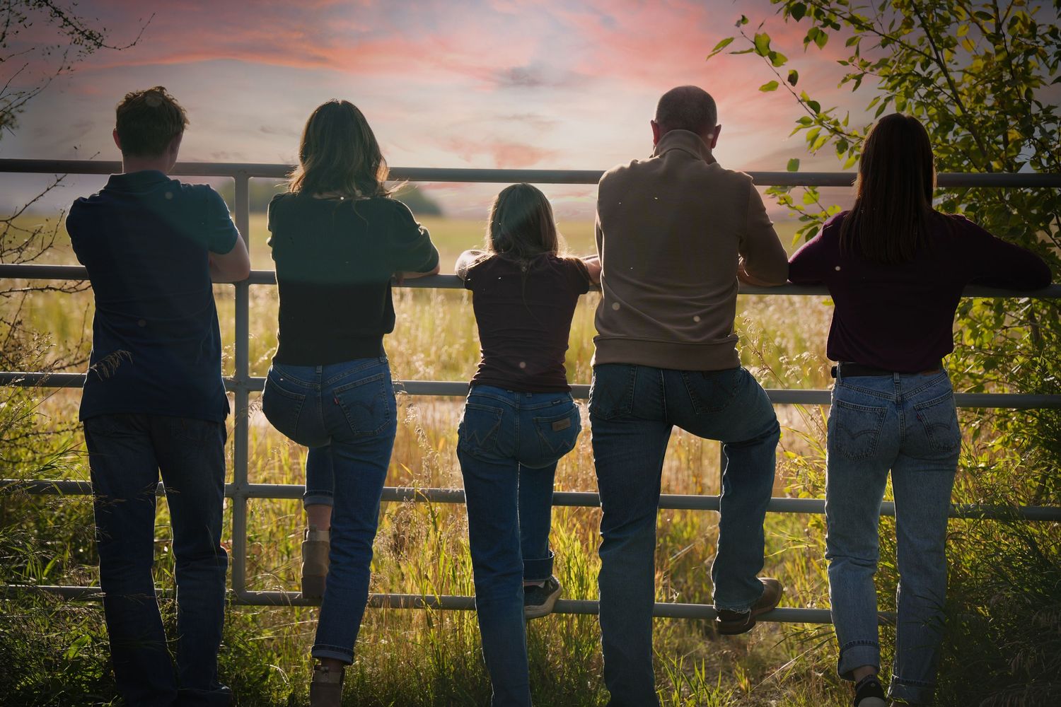 Silhouettes of people leaning against a fence during sunset over a scenic landscape.